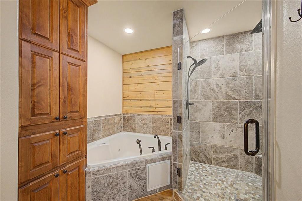 2789 Hanging Tree Road Bowie, TX 76230 - Photo 17 of 40 Built-in wood cabinetry, corner jetted tub, tiled tub surround, walk-in shower with glass enclosure, and pebble-tile shower floor