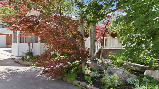 3120 North Apache Way Provo, UT 84604 - Photo 15 of 58 Landscaped front exterior featuring a screened porch, a red Japanese maple, mature deciduous trees, a rock garden, and a paved driveway leading to a garage with a white door
