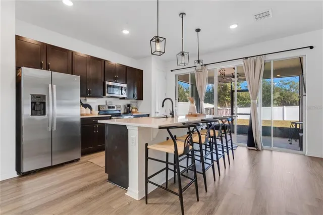 a kitchen with stainless steel appliances granite countertop a refrigerator a sink a stove a dining table and chairs with wooden floor