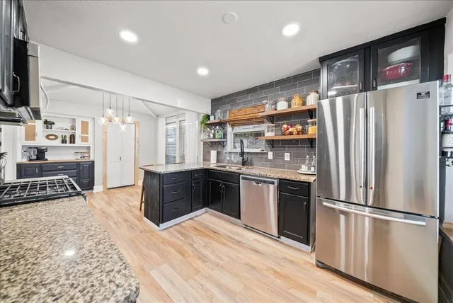 a kitchen with stainless steel appliances granite countertop a refrigerator a stove and a sink with wooden floor