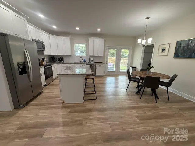 a kitchen with stainless steel appliances kitchen island granite countertop a refrigerator a stove a sink a dining table and chairs with wooden floor