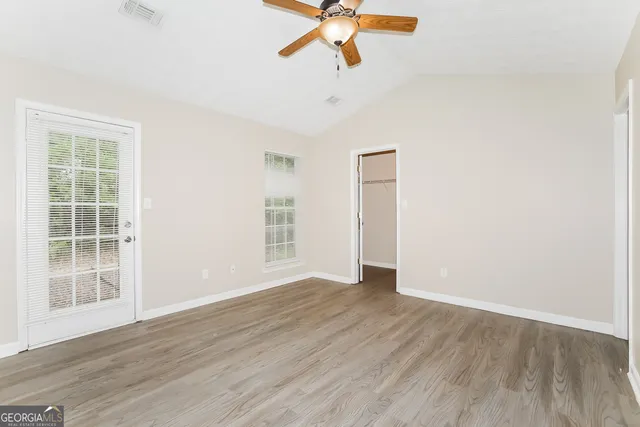 an empty room with wooden floor fan and windows