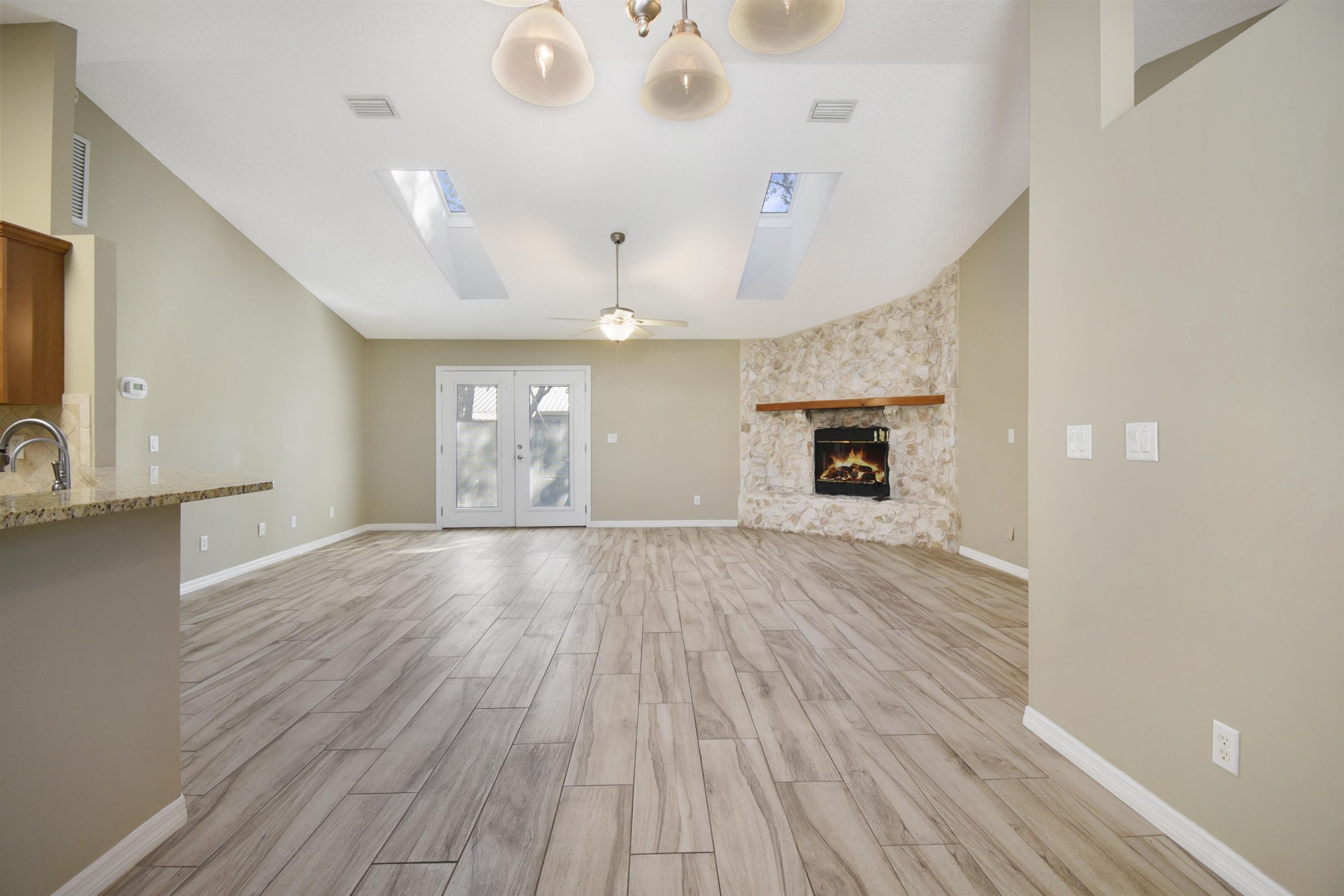317 Mystical Way St. Augustine, FL 32080 - Photo 4 of 25 Unfurnished living room with wood tiled floors, a fireplace, french doors, a skylight, and a ceiling fan