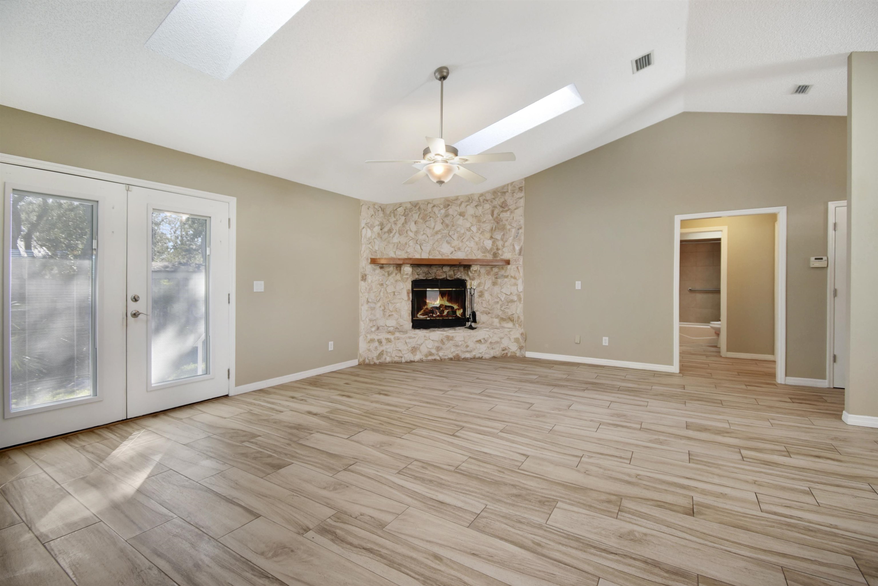 317 Mystical Way St. Augustine, FL 32080 - Photo 5 of 25 Unfurnished living room featuring a skylight, lofted ceiling, wood finish floors, a stone fireplace, and french doors