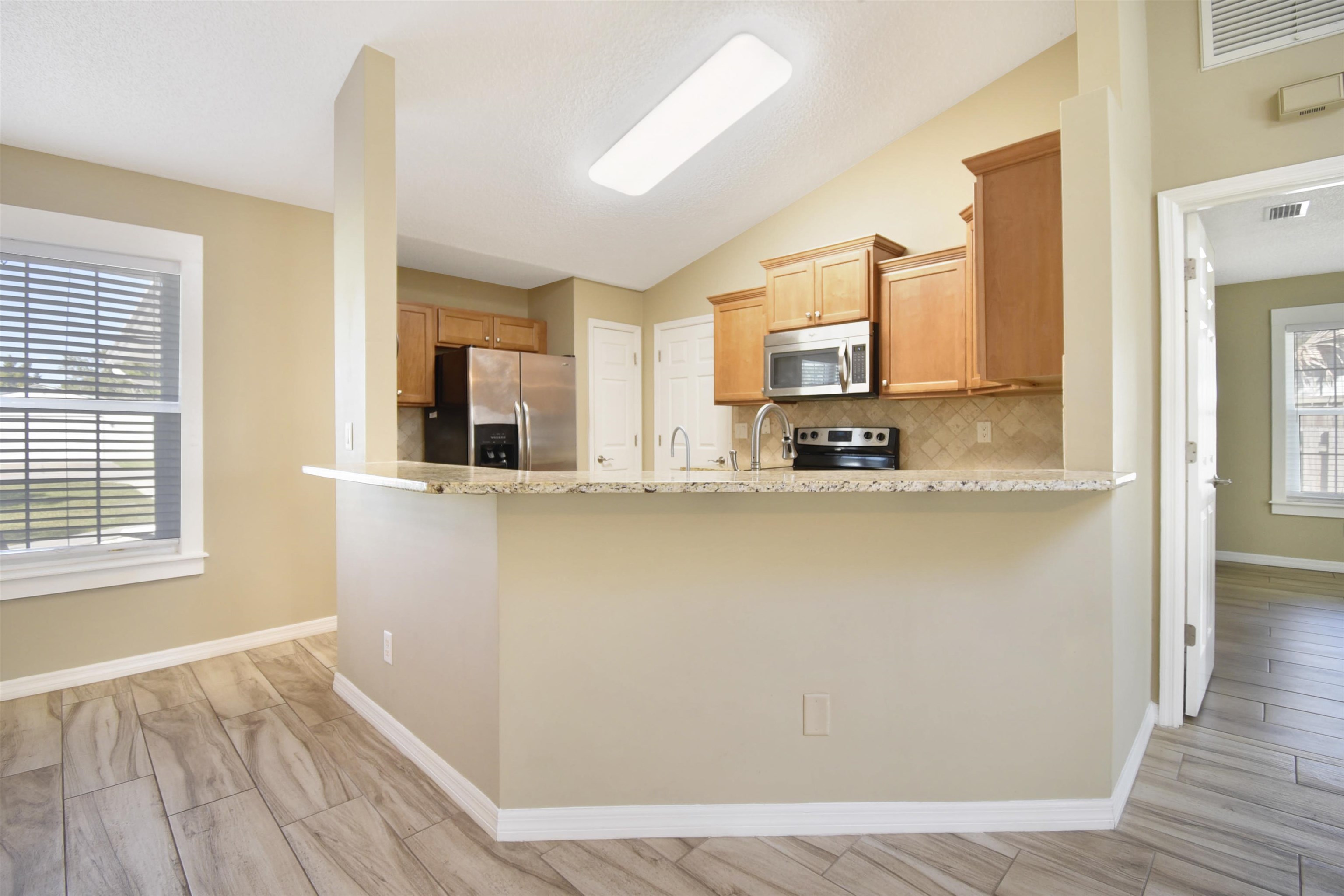 317 Mystical Way St. Augustine, FL 32080 - Photo 8 of 25 Kitchen featuring tasteful backsplash, appliances with stainless steel finishes, vaulted ceiling, light stone countertops, and wood tiled floors