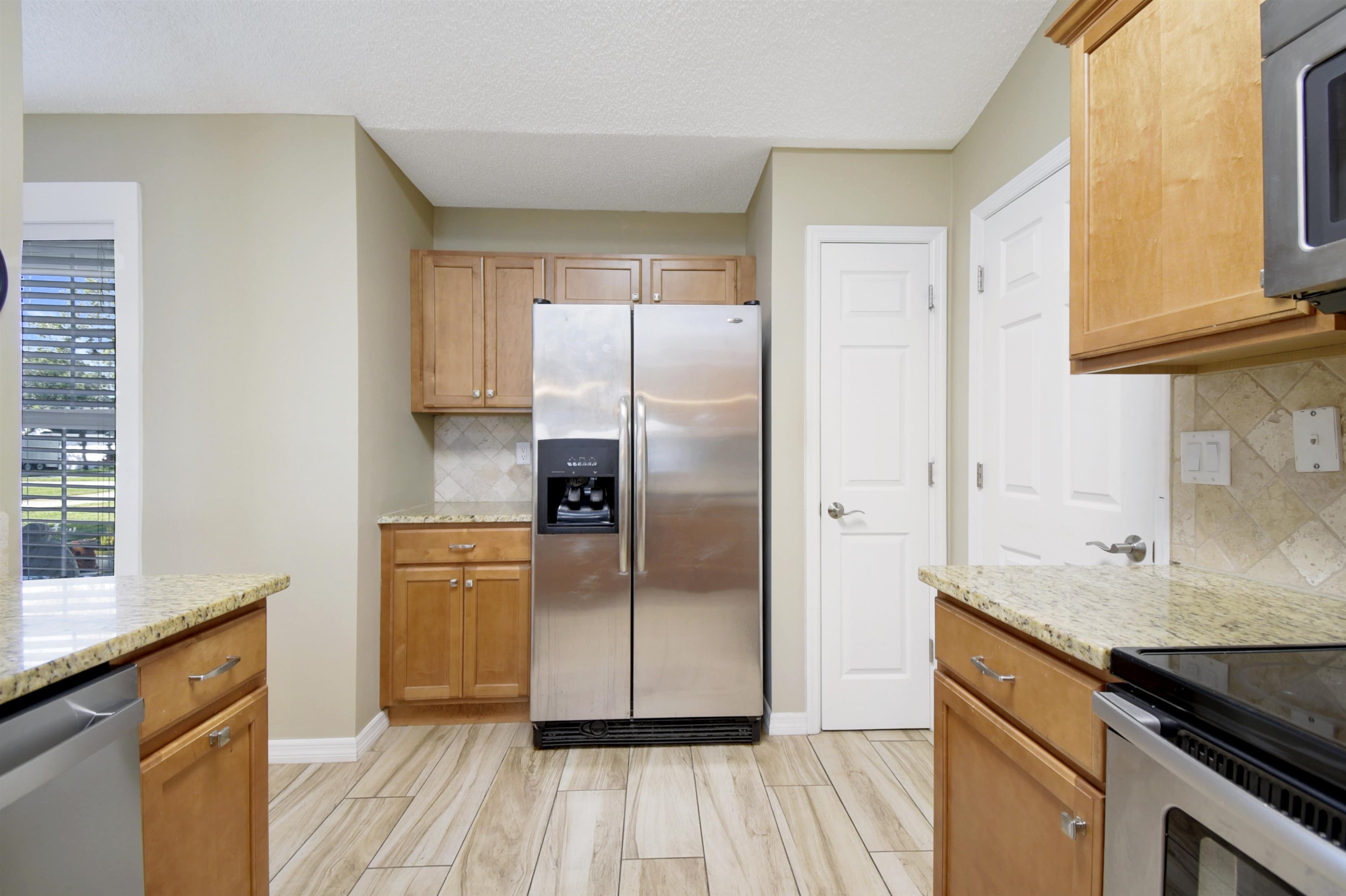 317 Mystical Way St. Augustine, FL 32080 - Photo 9 of 25 Kitchen featuring stainless steel appliances, backsplash, light stone countertops, wood finish floors, and brown cabinetry