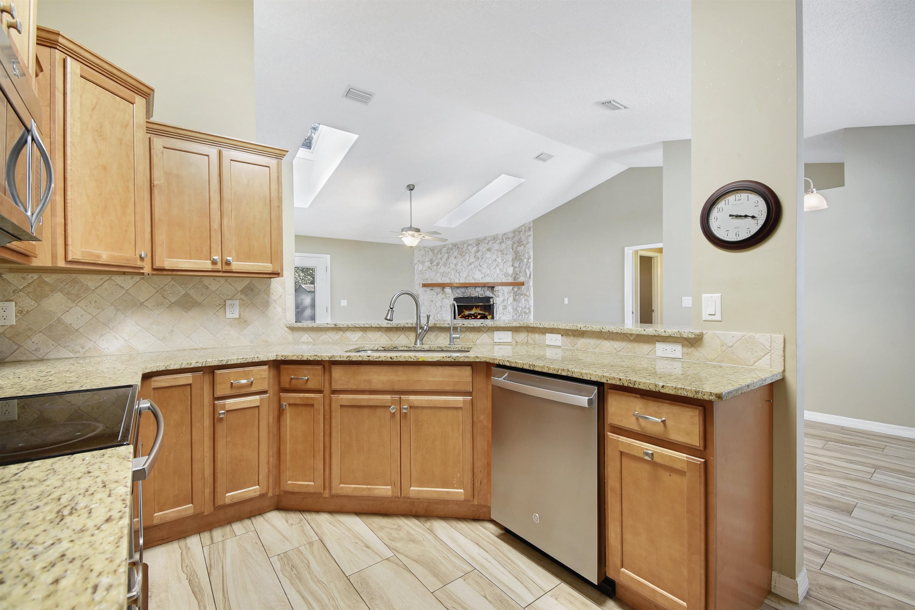 317 Mystical Way St. Augustine, FL 32080 - Photo 10 of 25 Kitchen featuring tasteful backsplash, light stone counters, a skylight, brown cabinetry, and lofted ceiling