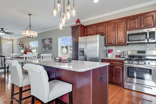 a kitchen with stainless steel appliances granite countertop a stove refrigerator a dining table and chairs with wooden floor