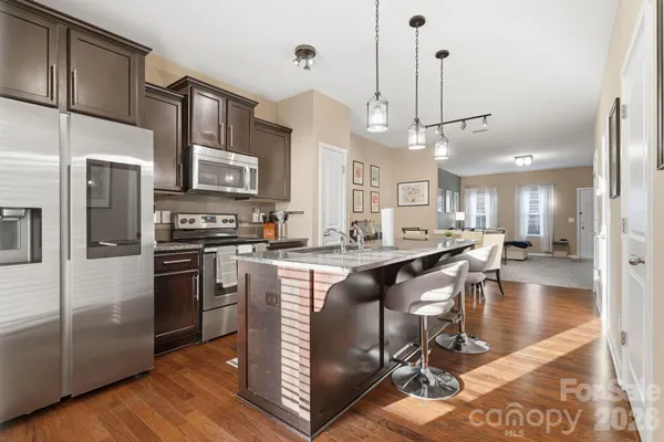 a kitchen with stainless steel appliances granite countertop a stove a refrigerator a oven a sink a dining table and chairs with wooden floor