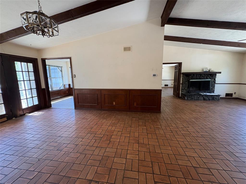 5454 Ranchero Lane Dallas, TX 75236 - Photo 6 of 24 Vaulted ceilings with exposed wood beams, brick-patterned flooring, wood wainscoting, and a stone fireplace