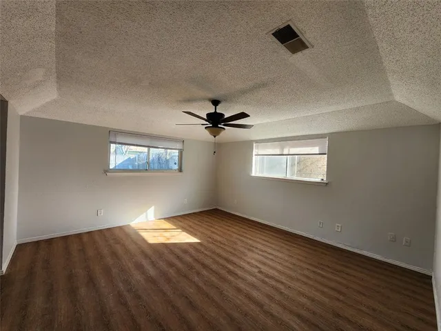 an empty room with wooden floor chandelier fan and windows