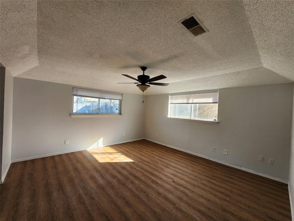 803 10th Street Princeton, TX 75407 - Photo 8 of 12 an empty room with wooden floor chandelier fan and windows