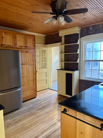 a view of a refrigerator in kitchen and an empty room with wooden floor
