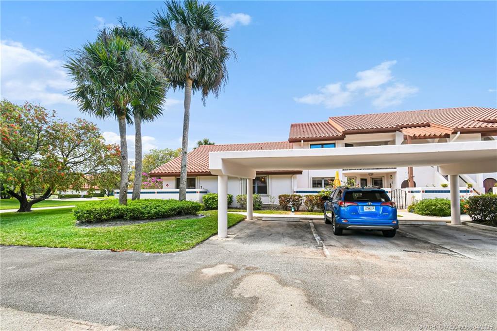 3401 Southeast Martinique Trace, Unit 101 Stuart, FL 34997 - Photo 3 of 51 a car parked in front of a brick house with a large tree