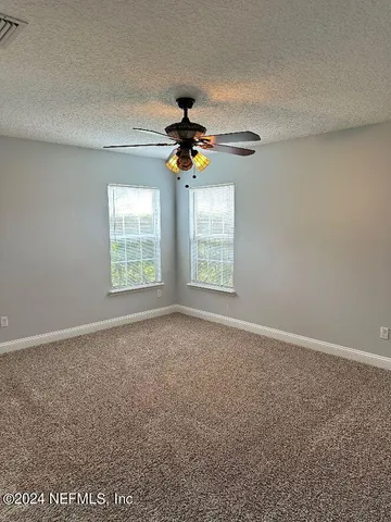 an empty room with windows and chandelier fan