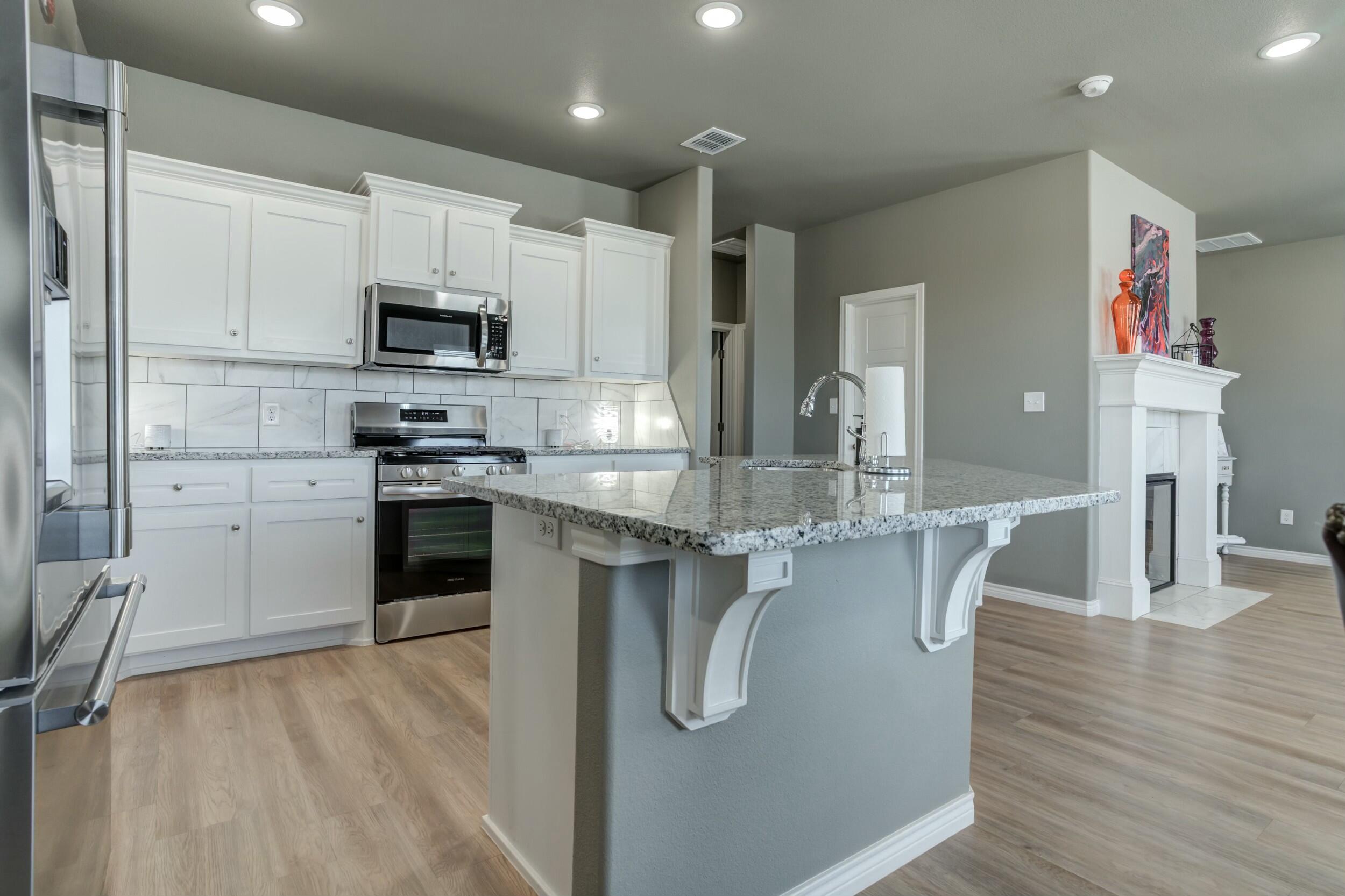 6928 11th Street Lubbock, TX 79416 - Photo 24 of 42 a kitchen with stainless steel appliances granite countertop a stove top oven a sink dishwasher a dining table and chairs with wooden floor