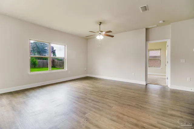 an empty room with wooden floor chandelier fan and windows