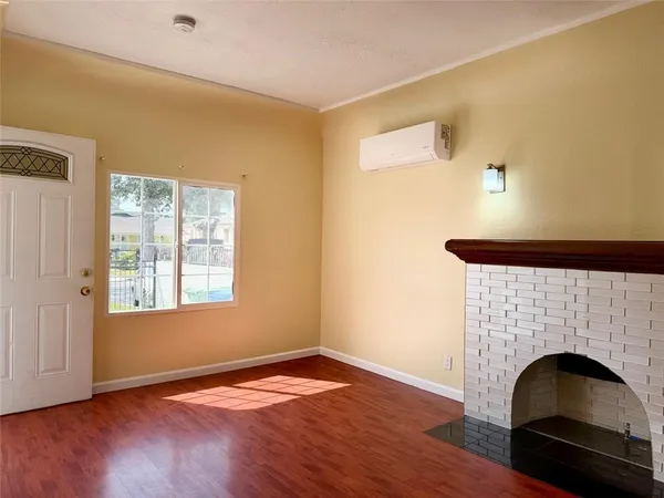 a view of an empty room with wooden floor fireplace and a window