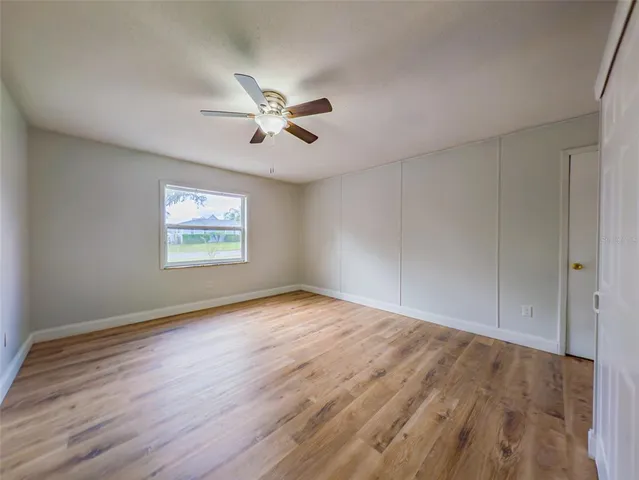 an empty room with wooden floor chandelier fan and windows