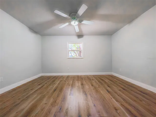 an empty room with wooden floor chandelier fan and windows