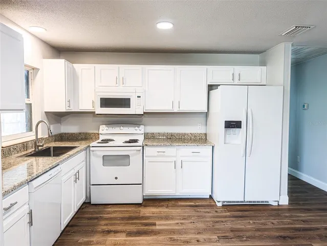 a kitchen with granite countertop a refrigerator stove and white cabinets