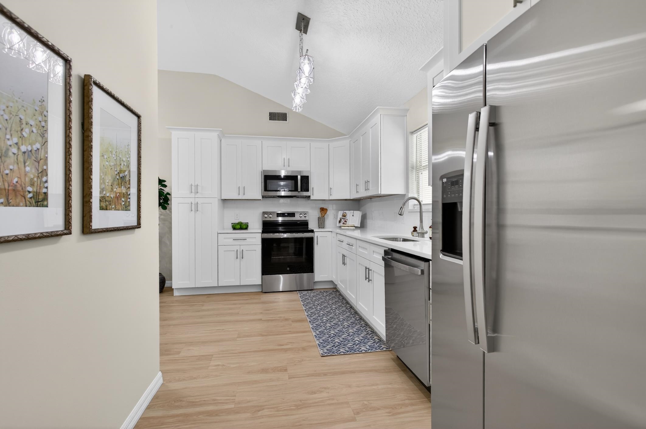 37 Madeore Street St. Augustine, FL 32084 - Photo 19 of 45 Kitchen with new stainless steel appliances, white cabinetry, vaulted ceiling, and light vinyl plank flooring.