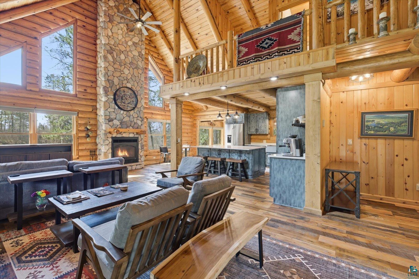 7185 Giants Ridge Road Embarrass, MN 55732 - Photo 8 of 47 Vaulted wood-paneled ceilings with exposed beams, a floor-to-ceiling stone fireplace, and wood-finish flooring