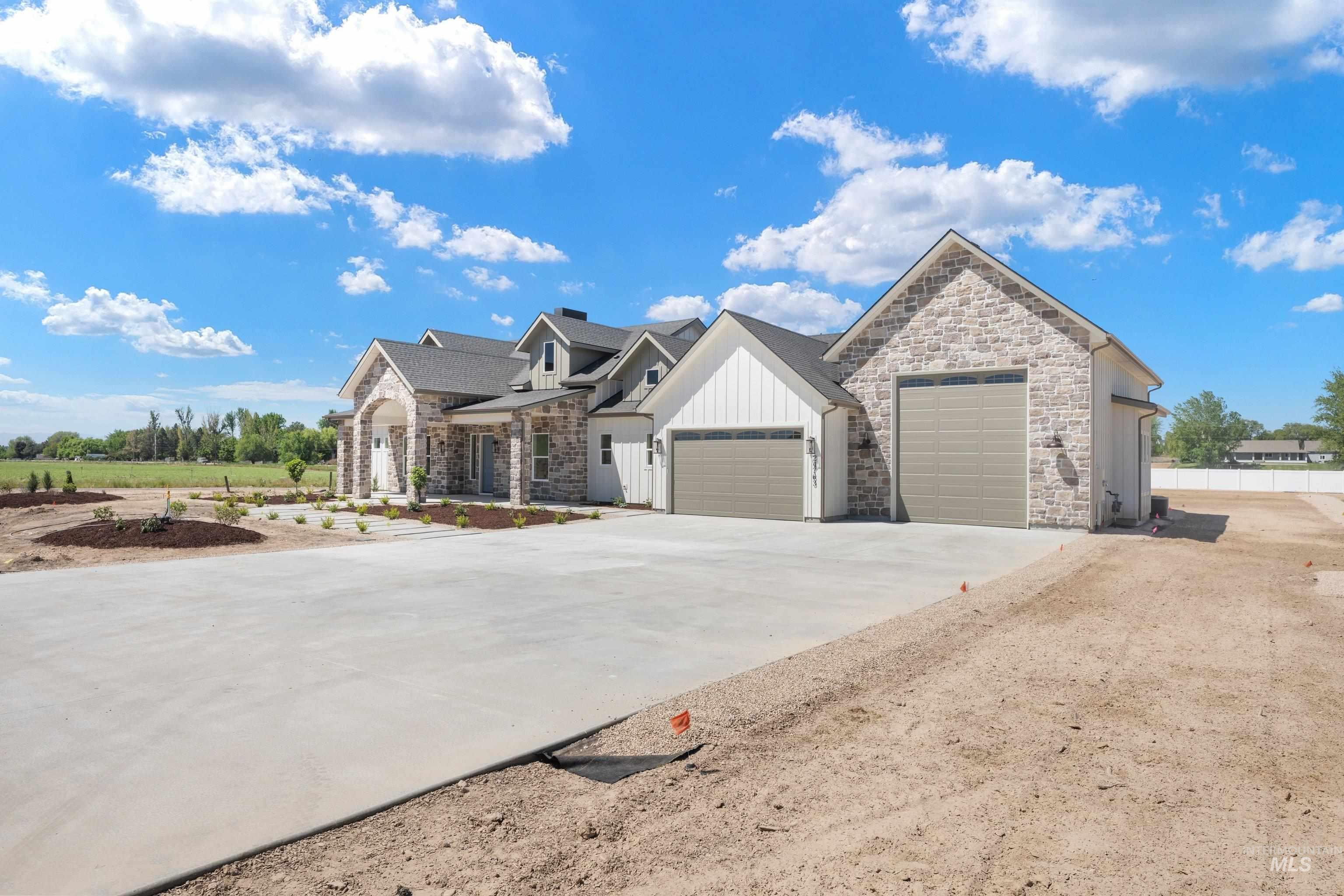 24821 Ardmore Court Caldwell, ID 83607 - Photo 5 of 43 Stone and board-and-batten exterior with a multi-car garage, featuring a concrete driveway and landscaped beds with young plantings