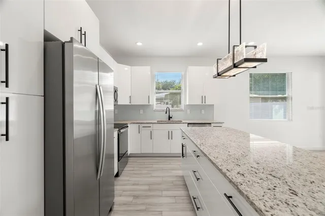 a kitchen with stainless steel appliances granite countertop a refrigerator a sink dishwasher a stove and white cabinets with wooden floor