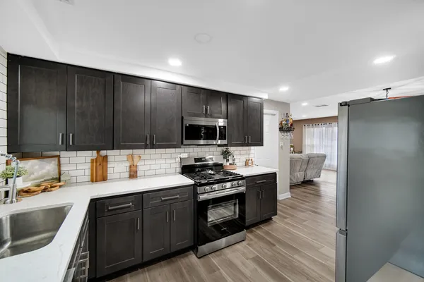 a kitchen with stainless steel appliances a stove top oven a sink dishwasher and a refrigerator with wooden floor