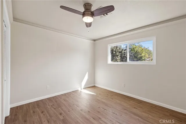 an empty room with wooden floor ceiling fan and window
