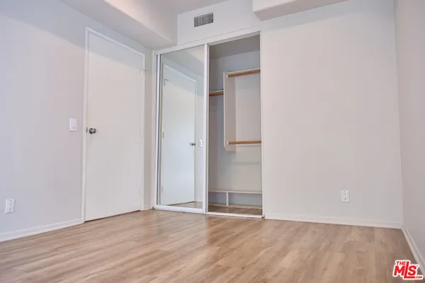 a view of an empty room with wooden floor and closet