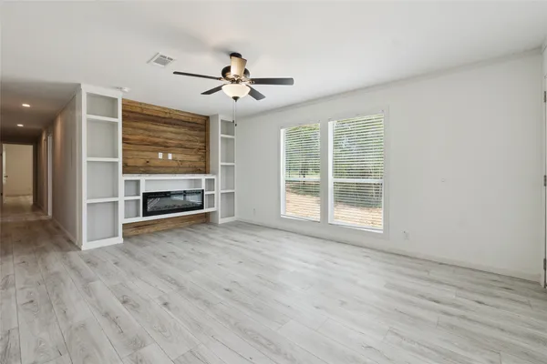 an empty room with wooden floor ceiling fan and windows