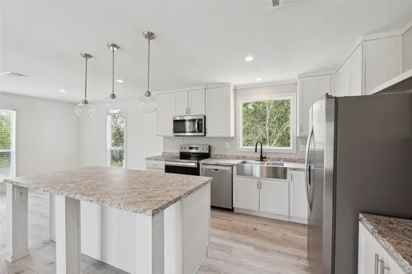a kitchen with stainless steel appliances granite countertop a refrigerator a stove a sink and a granite counter tops with white cabinets