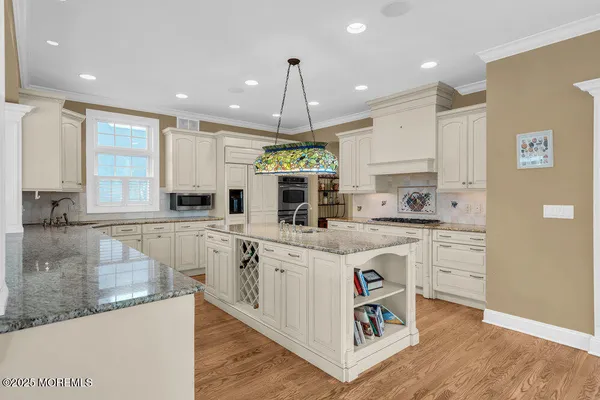 a large kitchen with kitchen island granite countertop a stove a sink a refrigerator and white cabinets with wooden floor