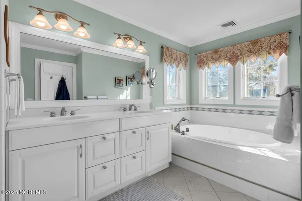 a spacious bathroom with a double vanity sink a large mirror a bathtub and next to a window