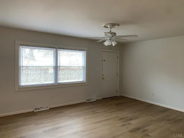 an empty room with chandelier fan and windows