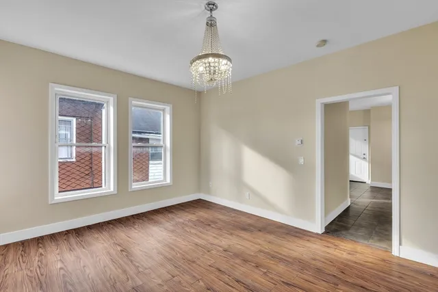 an empty room with wooden floor chandelier and windows