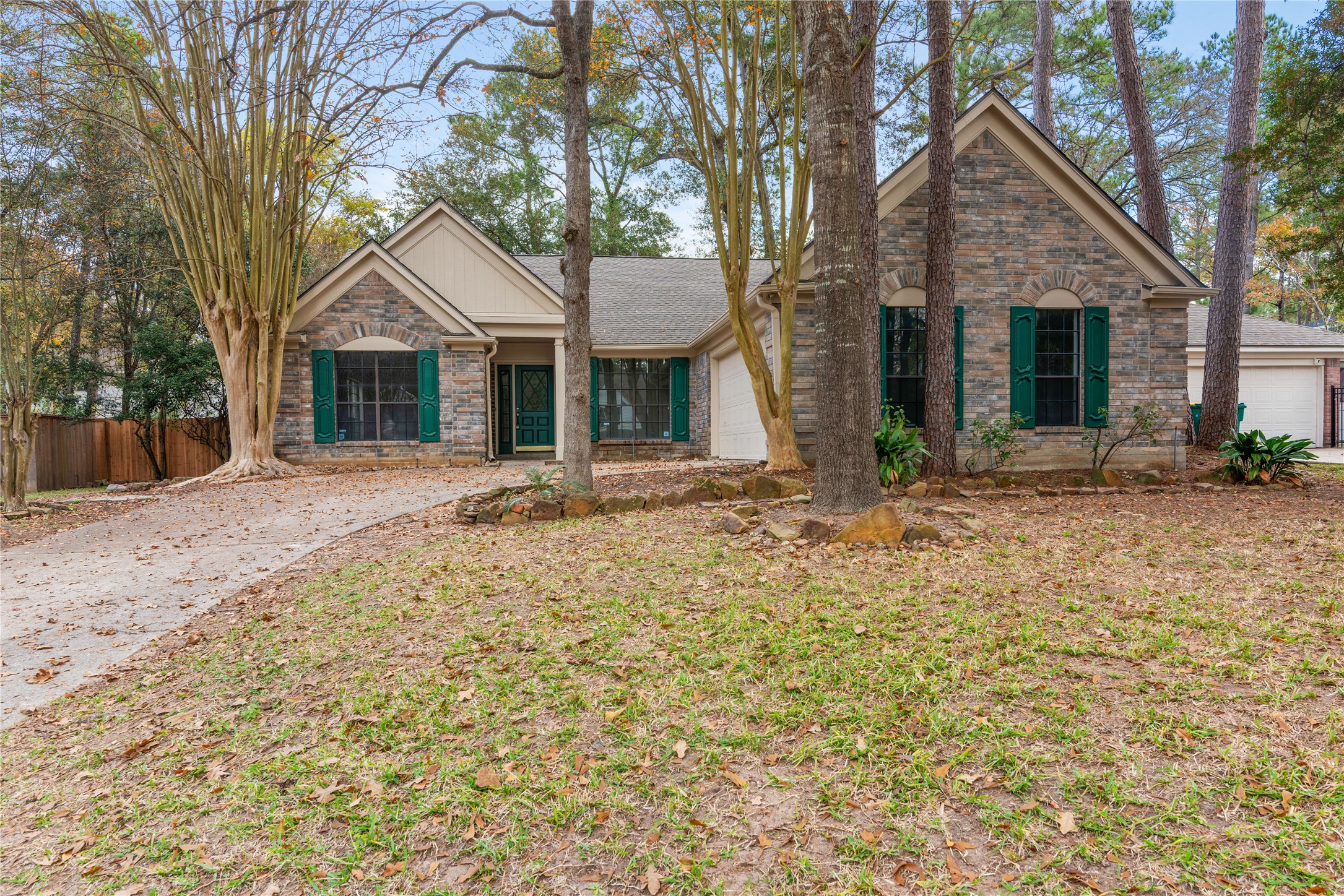 10 White Fawn Drive Spring, TX 77381 - Photo 2 of 25 Charming single-story home with a brick facade and green shutters, nestled among mature trees. It features a spacious front yard and a curved driveway leading to an attached garage. The peaceful, wooded setting provides a serene atmosphere.