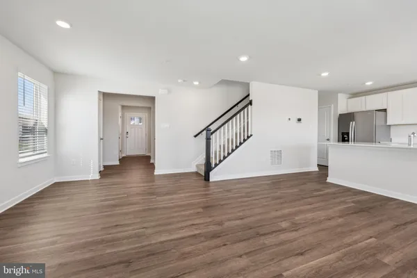 a view of an empty room with wooden floor and a kitchen