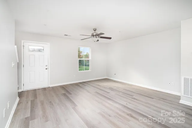 an empty room with wooden floor ceiling fan and windows