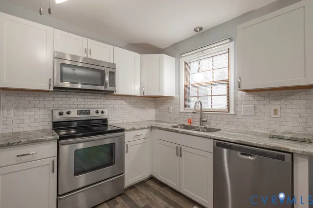 a kitchen with granite countertop white cabinets sink and stainless steel appliances