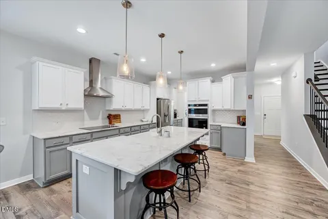 a large kitchen with stainless steel appliances kitchen island granite countertop a stove a refrigerator a sink a dining table and chairs with wooden floor