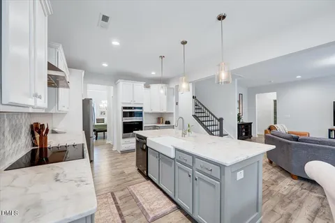 a living room with stainless steel appliances kitchen island granite countertop a sink a stove and a wooden floors