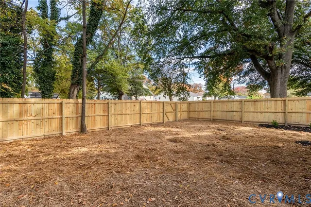a view of a yard with large trees and a wooden fence
