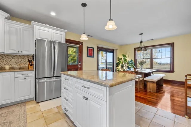 a kitchen with stainless steel appliances granite countertop a refrigerator a sink dishwasher a dining table and chairs with wooden floor