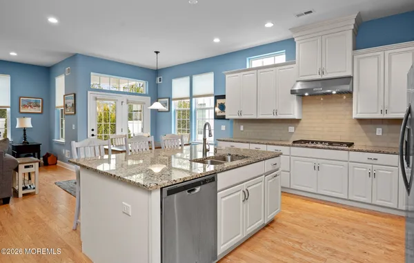 a kitchen with granite countertop sink stove and white cabinets with wooden floor
