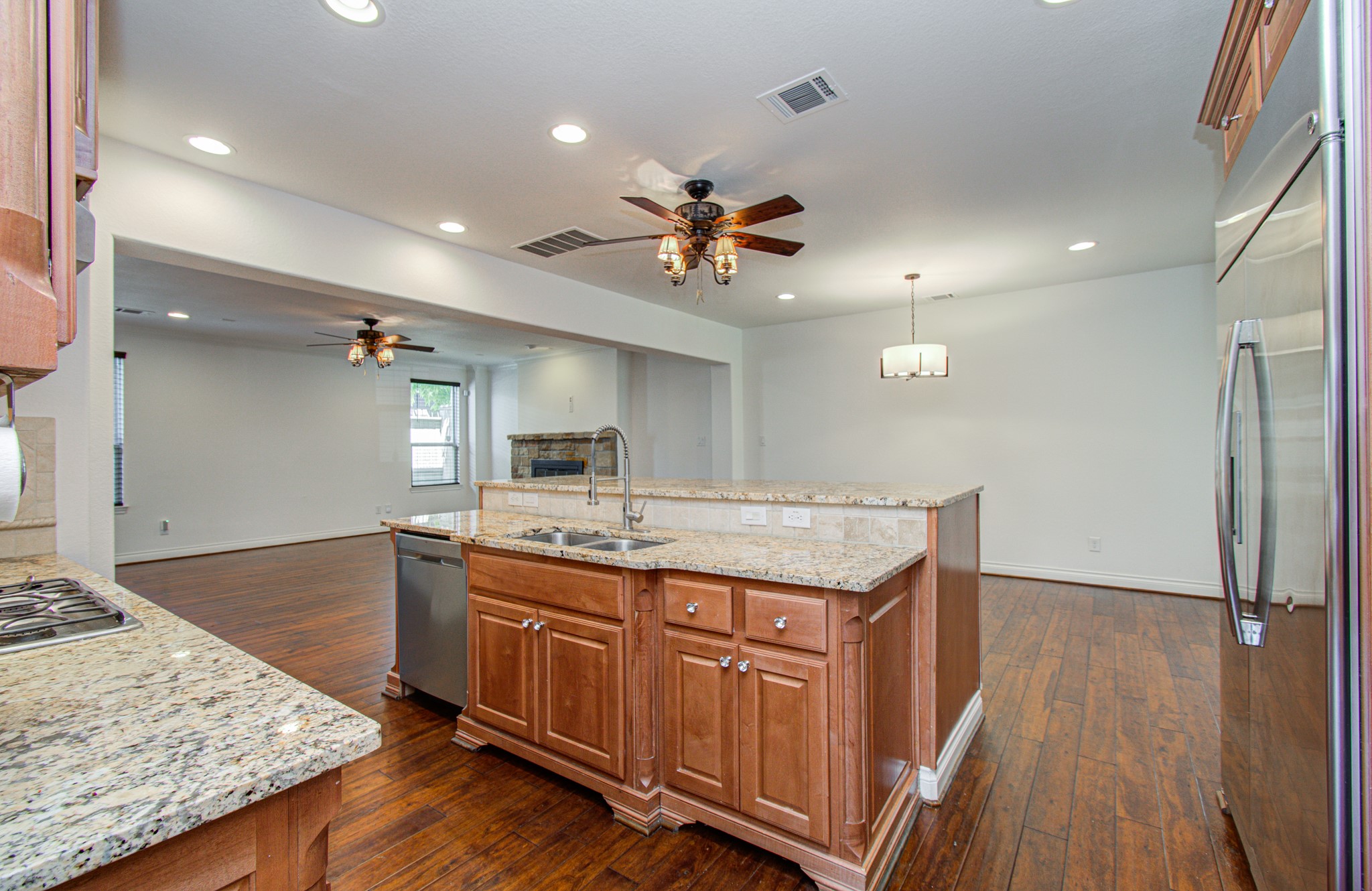 6621 North Main Street Houston, TX 77009 - Photo 13 of 41 This spacious open-concept kitchen features granite countertops, an island with a sink, modern appliances, and hardwood flooring. The area seamlessly connects to a living space with ceiling fans and ample lighting, creating a warm, inviting atmosphere.