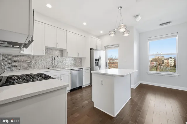 a kitchen with stainless steel appliances a stove a sink dishwasher a refrigerator and white cabinets with wooden floor