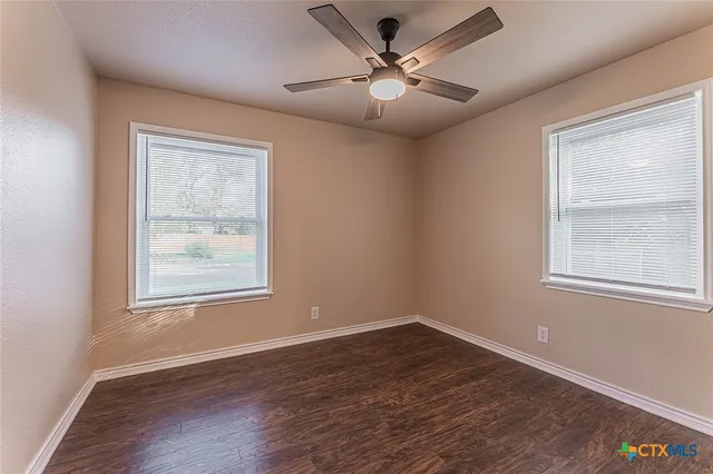 an empty room with wooden floor fan and windows